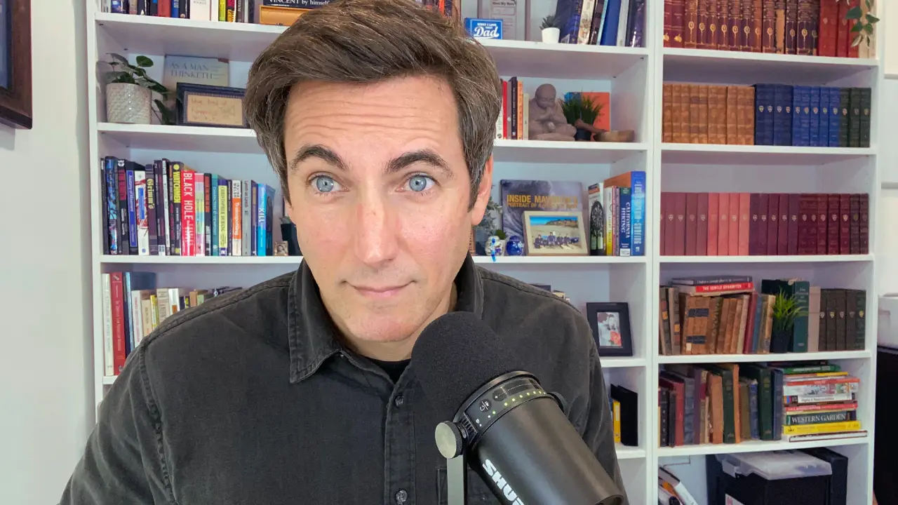 Corbett Uzel recording educational mortgage content in his office with bookshelf background and microphone